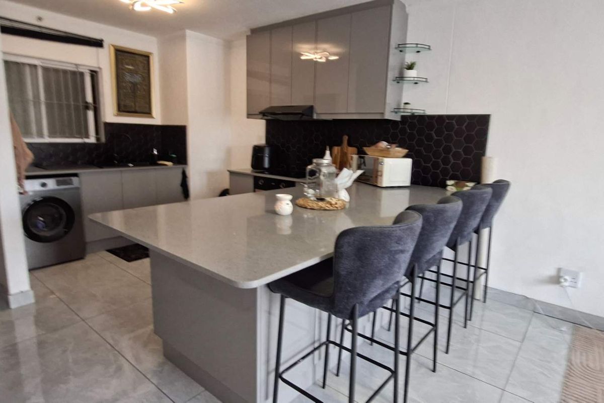 Modern kitchen featuring a central island with breakfast bar seating, sleek grey cabinetry, quartz countertops, and a stylish hexagonal tile backsplash.