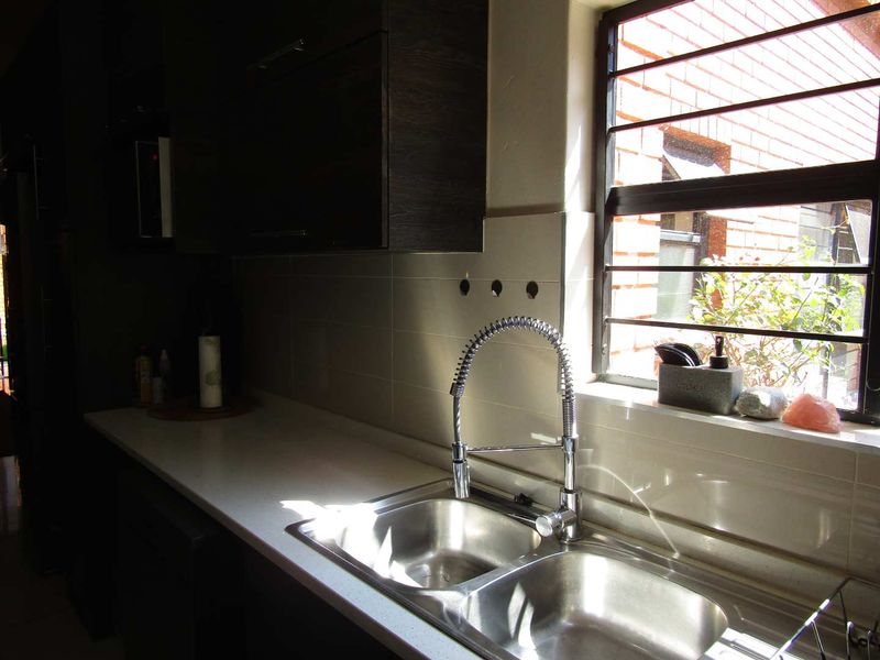 A functional kitchen area featuring a double stainless steel sink with a modern gooseneck mixer tap and tiled backsplash.