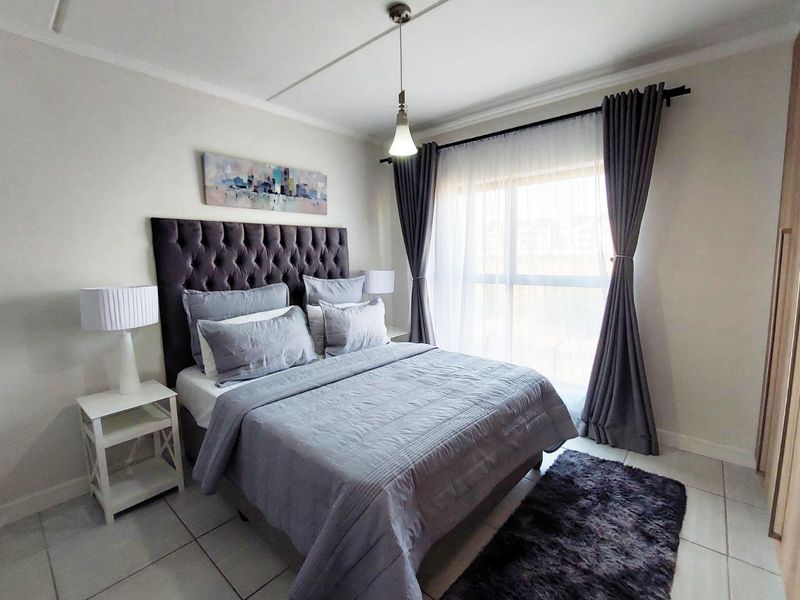 A well-maintained bedroom featuring tiled flooring, a built-in wardrobe, and a large window allowing for natural light.