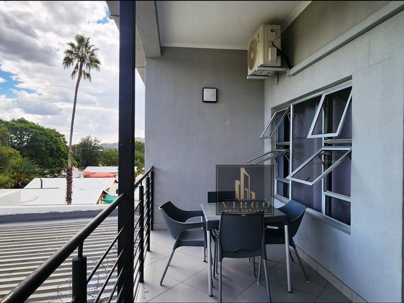 A covered balcony featuring tiled flooring, a metal safety railing, and a wall-mounted air conditioning unit, offering an elevated outdoor space.