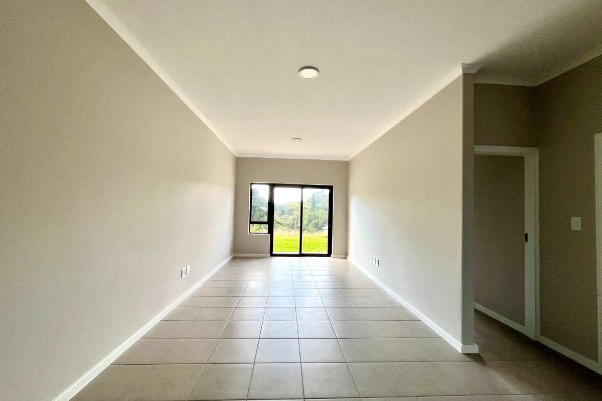 A bright, empty living area featuring neutral tiled flooring, recessed lighting, and a sliding glass door providing access to the outdoors.