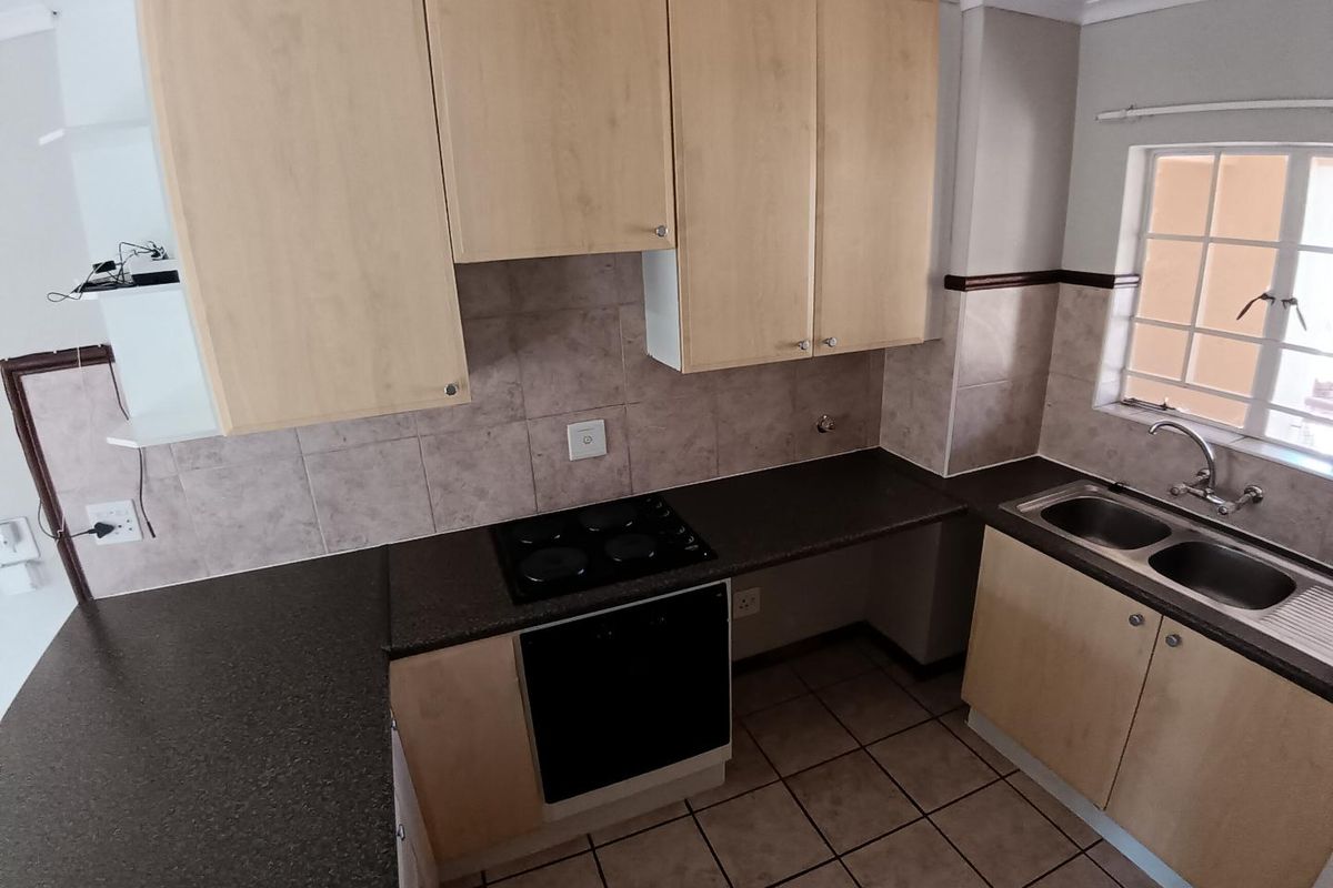 A functional kitchen featuring light wood-look cabinetry, dark countertops, an integrated electric oven and hob, and a double stainless steel sink.