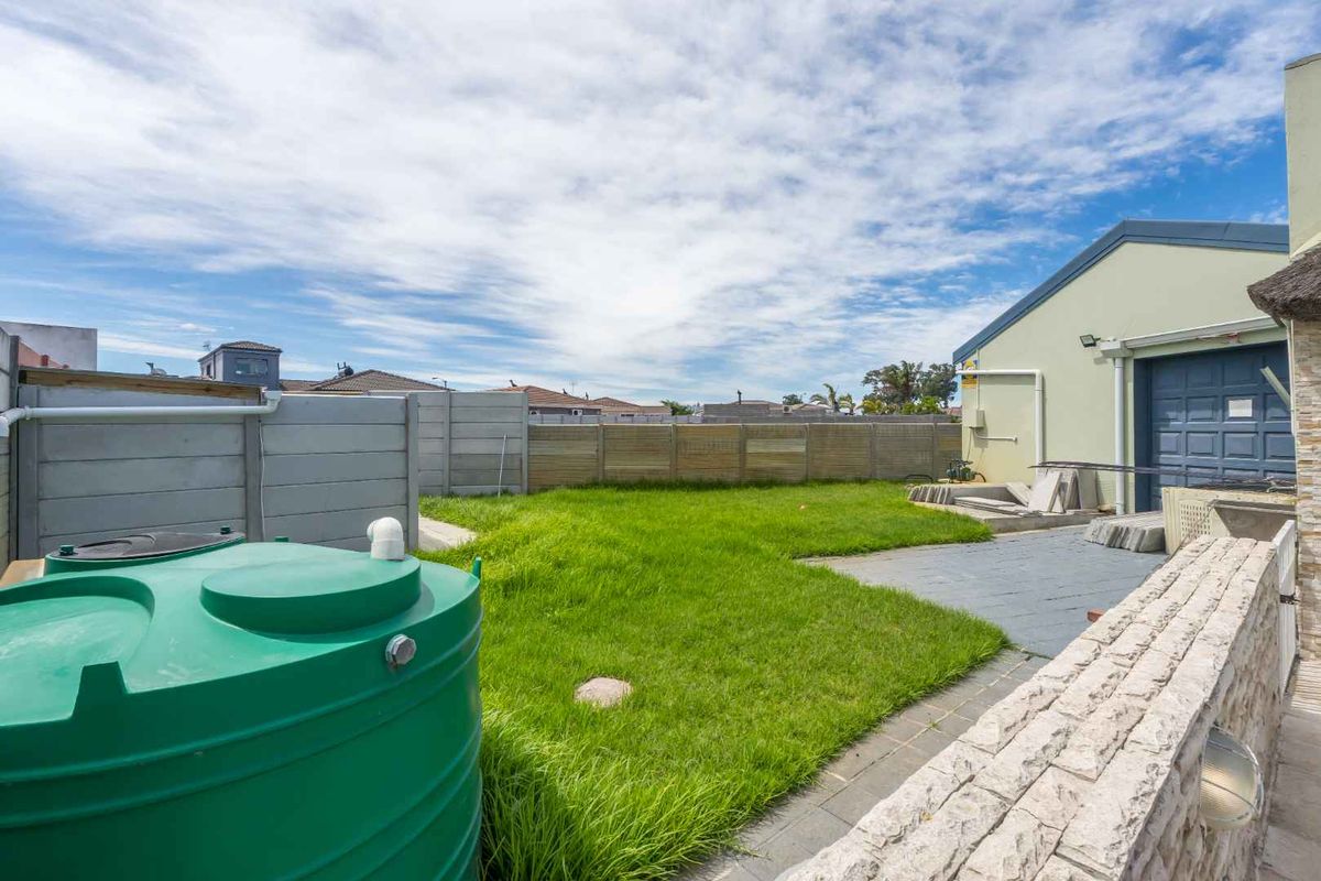 A rear garden area featuring a lawn, paved patio section, perimeter boundary wall, and a large water storage tank.