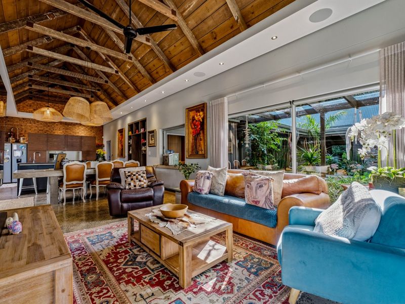 Spacious open-plan living and kitchen area featuring a dramatic vaulted timber ceiling, exposed trusses, polished concrete floors, and large sliding doors opening to the garden.