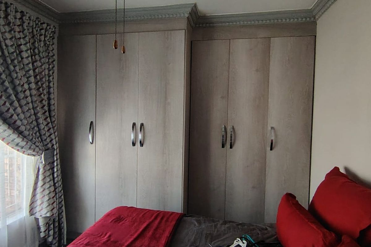 A bedroom featuring floor-to-ceiling built-in cupboards with a modern wood-grain finish and decorative crown molding.