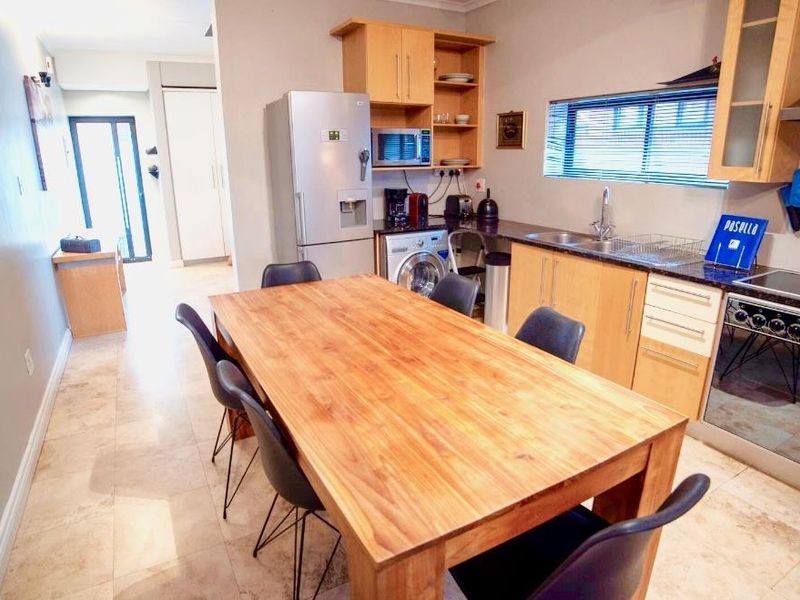 Open-plan kitchen and dining area featuring light wood cabinetry, granite countertops, built-in appliances, and tiled flooring throughout.