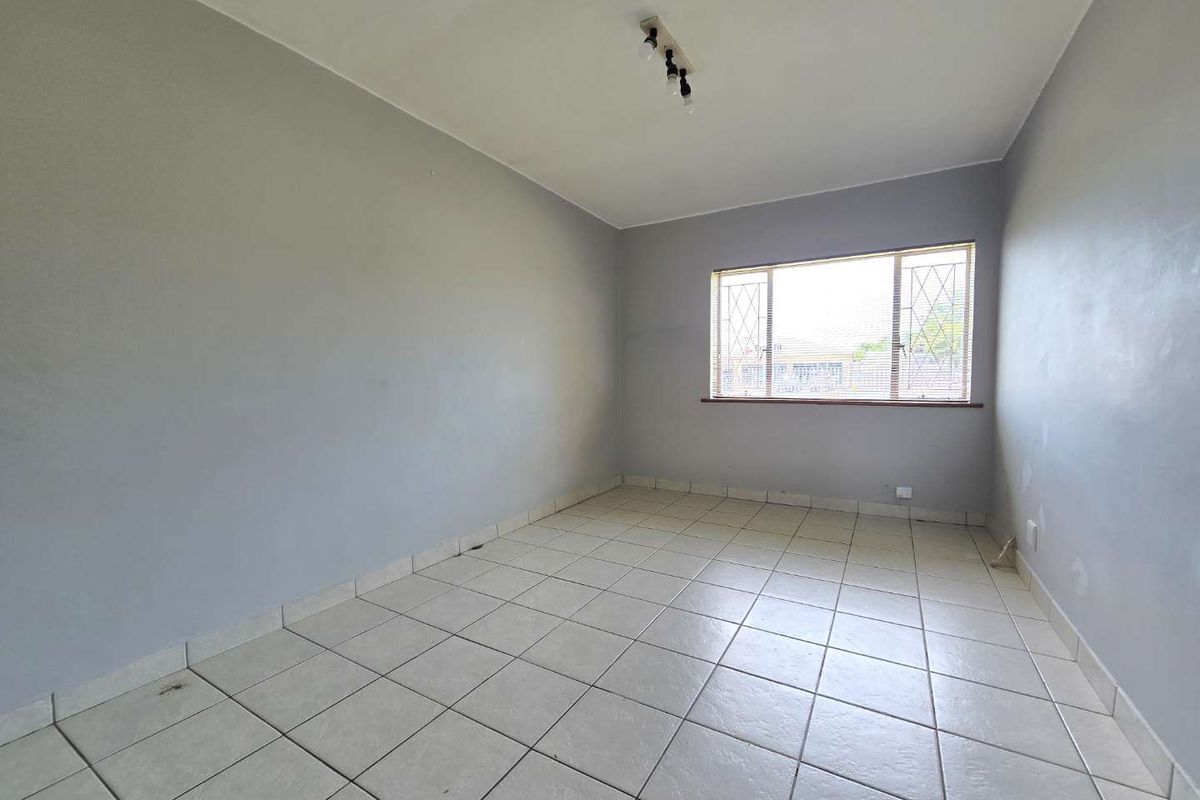An empty bedroom featuring tiled flooring, a window with security bars, and a ceiling-mounted light fixture, ready for personalization.