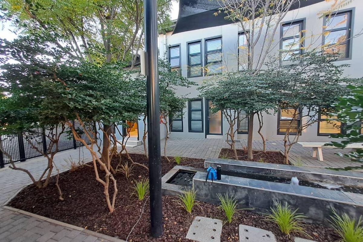 A well-maintained rear courtyard featuring a modern water feature, paved flooring, and established landscaping, providing a pleasant outdoor space for the office property.