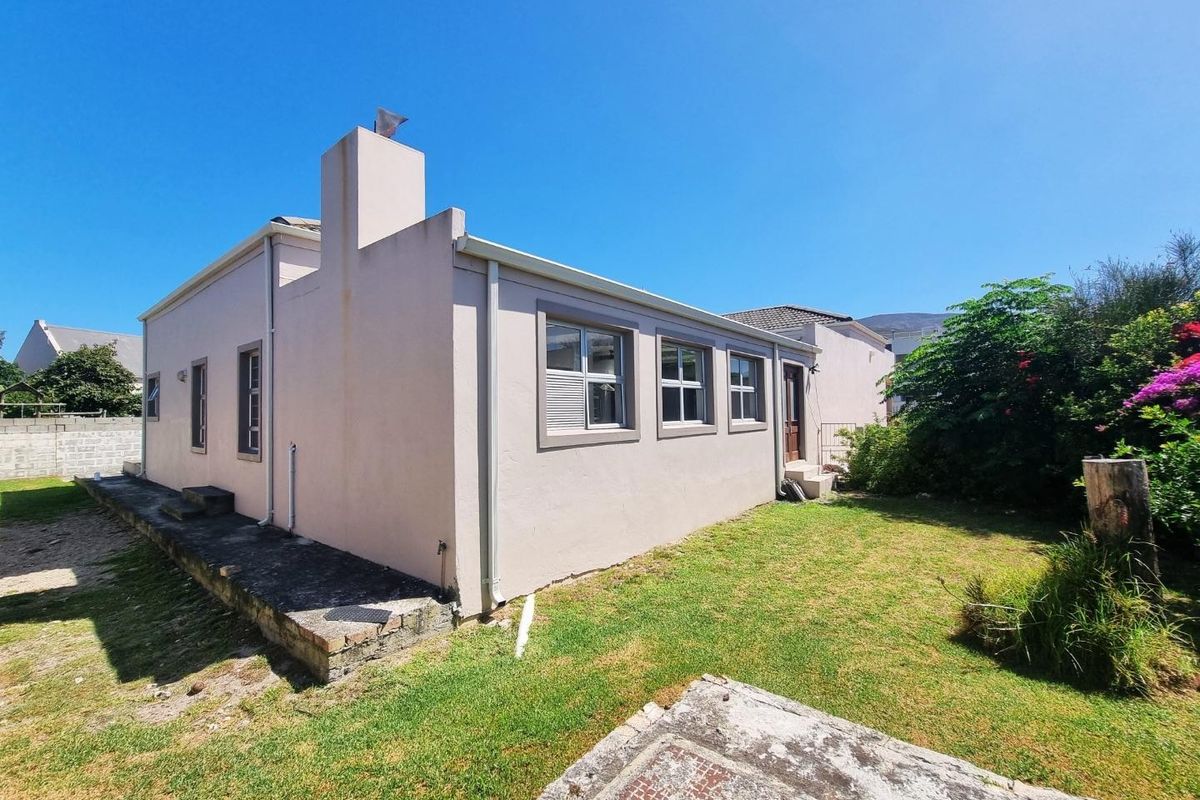 Rear view of the house featuring a lawned garden, concrete pathway, and exterior chimney stack.