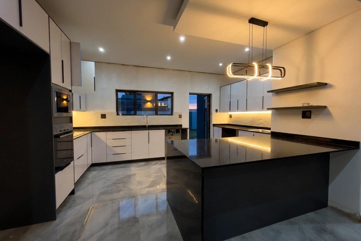 Modern kitchen featuring sleek white cabinetry, dark stone countertops, a central island, built-in appliances, and contemporary pendant lighting.