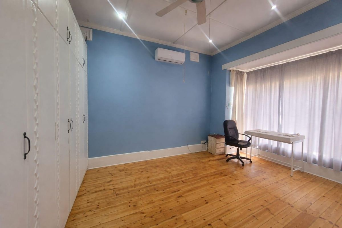 A bedroom featuring polished timber flooring, built-in cabinetry, a ceiling fan, and a wall-mounted air conditioning unit.