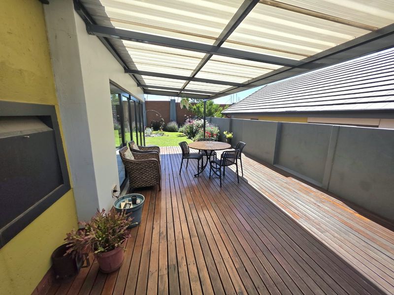 A well-maintained covered timber deck patio featuring a built-in braai, sliding door access, and views over the rear garden.