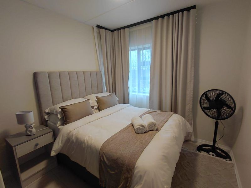 A cozy bedroom featuring neutral wall tones, floor-to-ceiling curtains, and a window providing natural light.