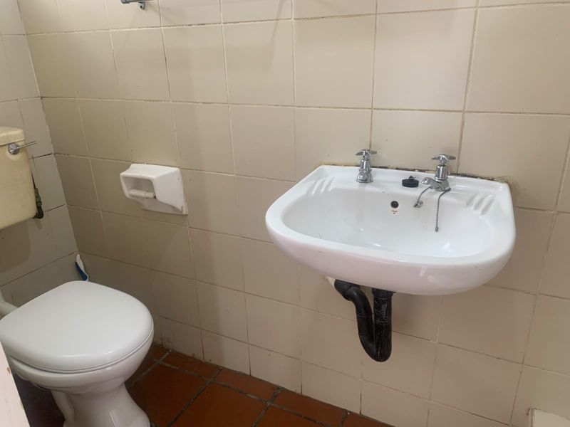 A dated bathroom featuring a wall-mounted basin, standard toilet, and tiled surfaces, offering potential for modernization and renovation.