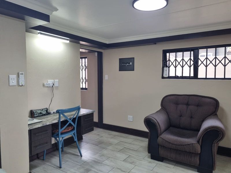 A functional living area featuring tiled flooring, a built-in desk workspace, and security bars on the windows.