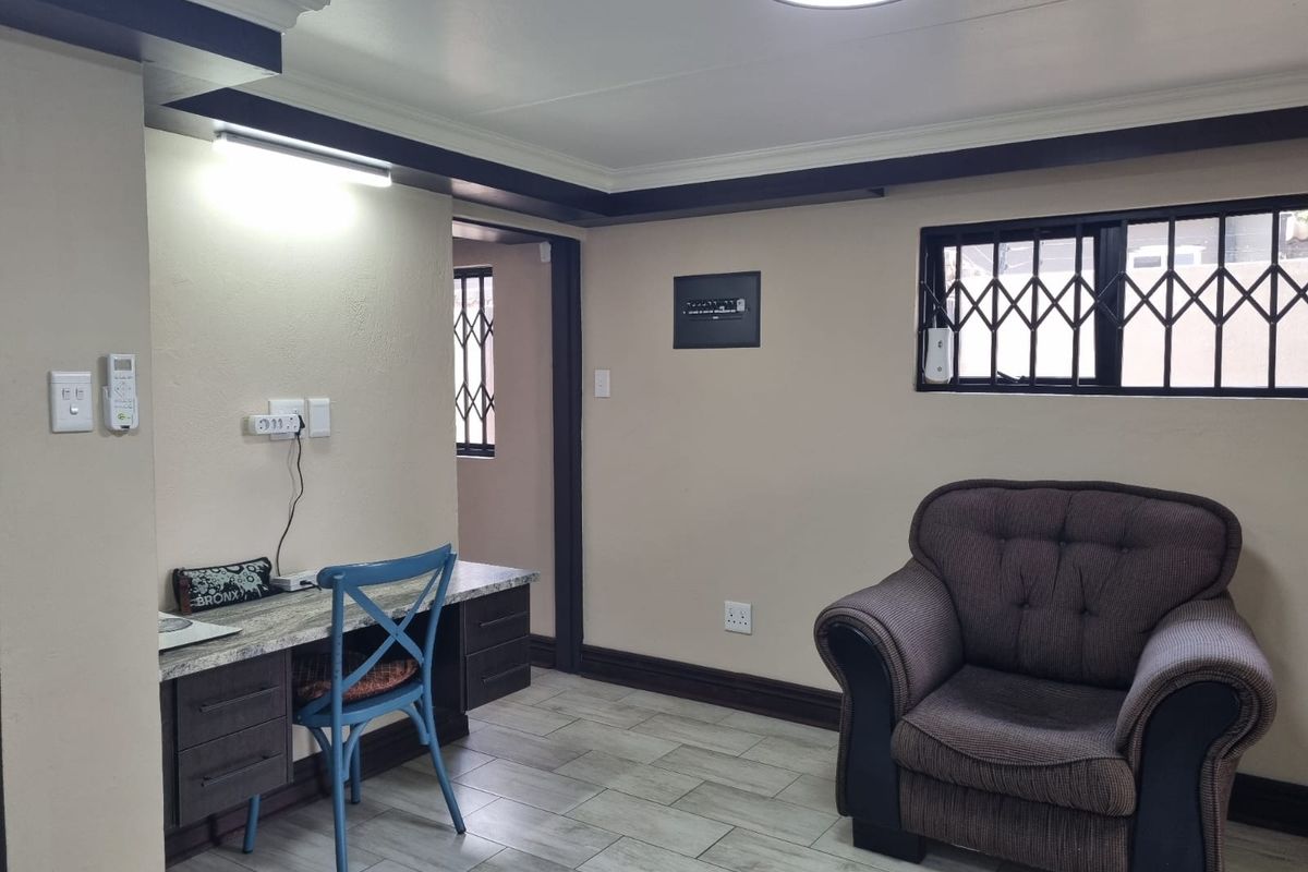 A functional living area featuring tiled flooring, a built-in desk workspace, and security bars on the windows.