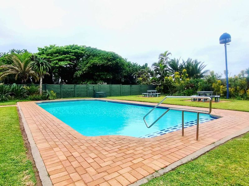 A well-maintained communal swimming pool area featuring brick paving, a stainless steel handrail, and surrounding landscaped garden space.