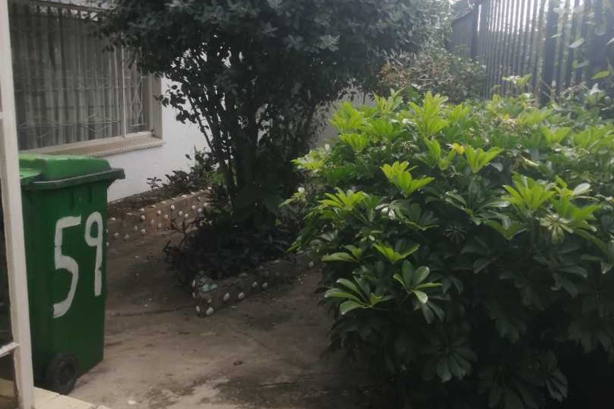 A view of the property's exterior side area featuring paved flooring, established garden beds, and perimeter security fencing.