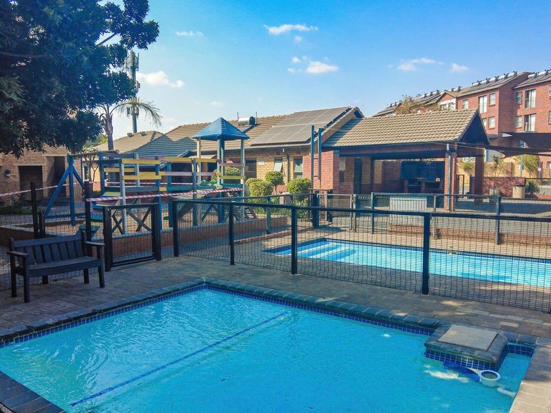 Communal apartment complex pool area featuring a swimming pool, paved deck, safety fencing, and a covered outdoor entertainment space.