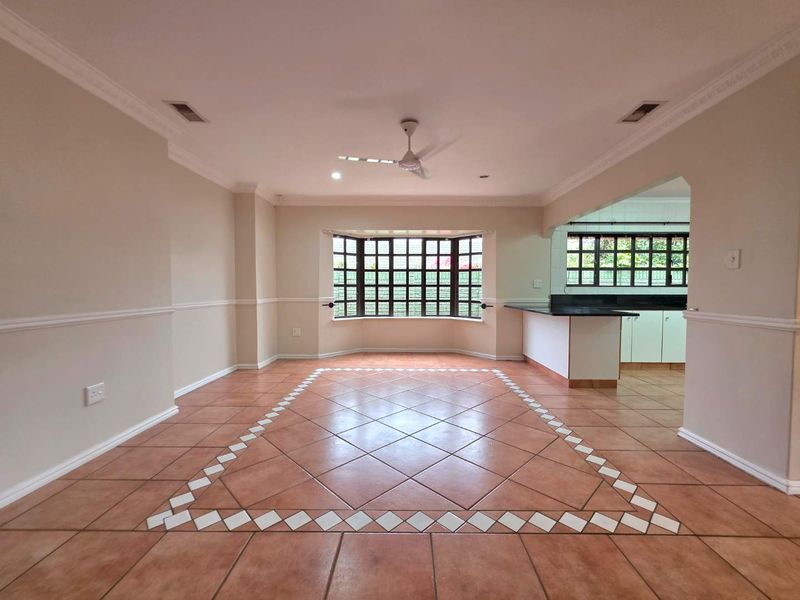 Spacious open-plan living and dining area featuring tiled floors with decorative inlay, a bay window, and a breakfast bar connecting to the kitchen.