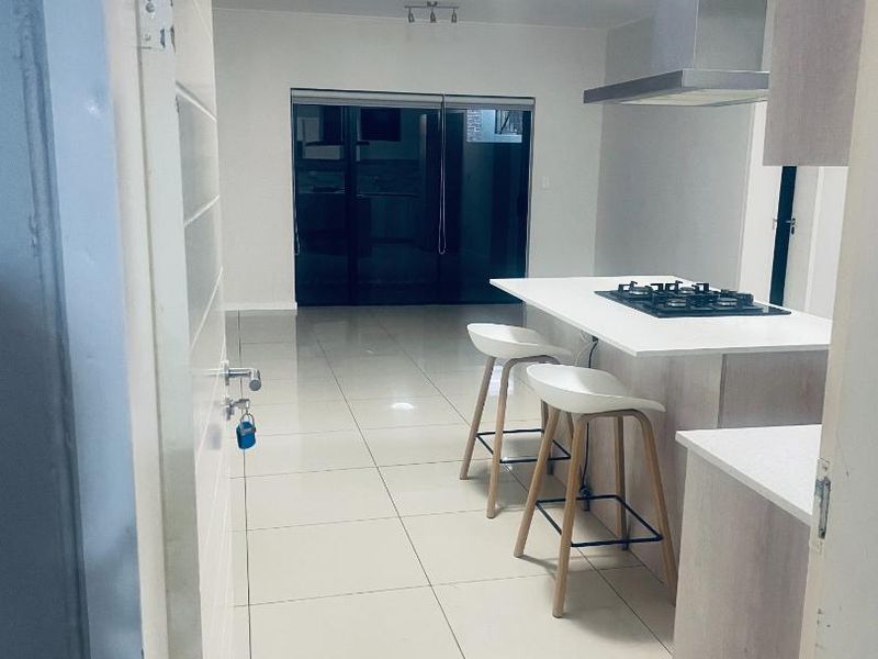 Modern open-plan living area featuring a kitchen island with a gas hob, stainless steel extractor fan, and large sliding glass doors leading outdoors.