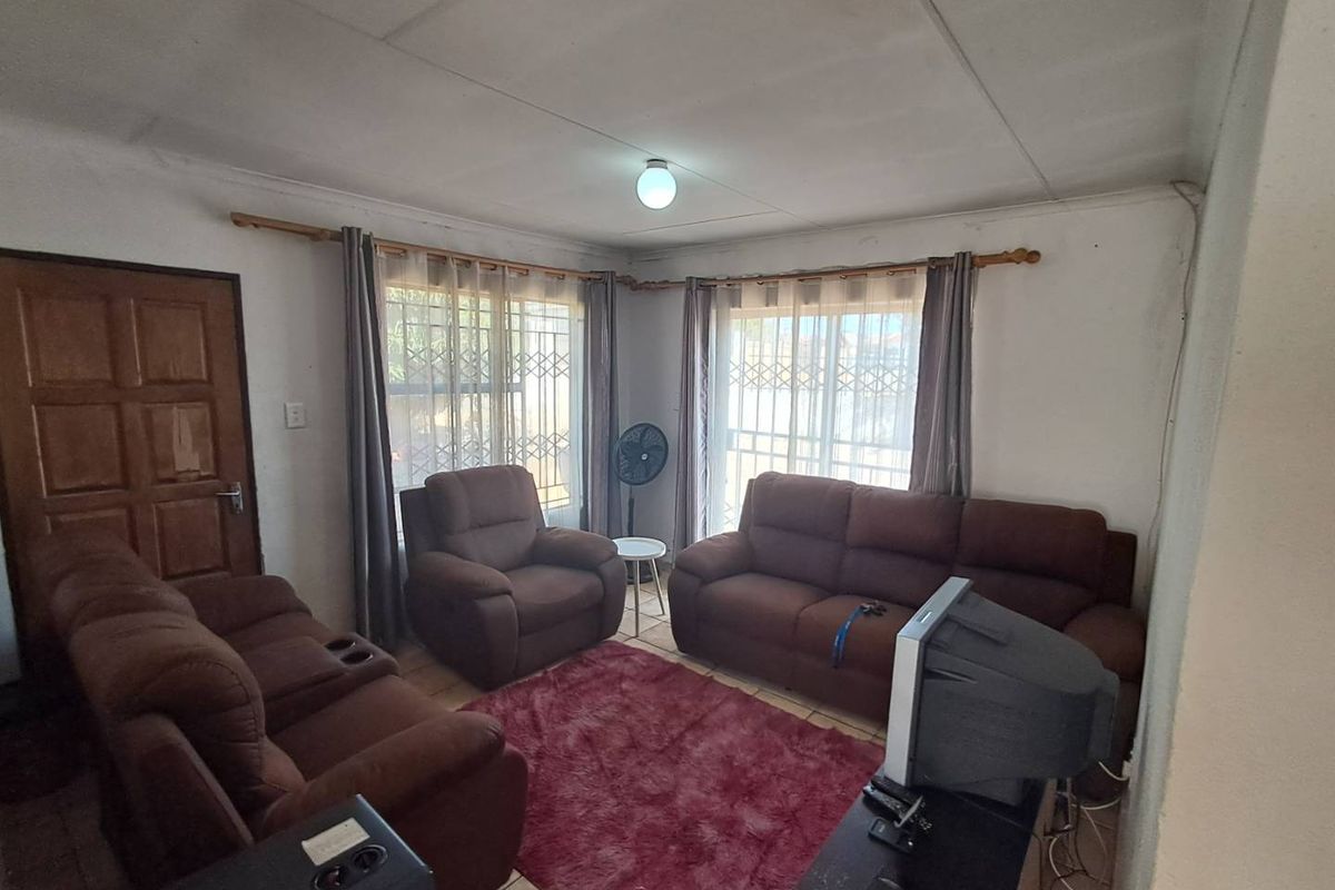 A living room featuring tiled flooring, large windows with security gates, and a standard ceiling finish.