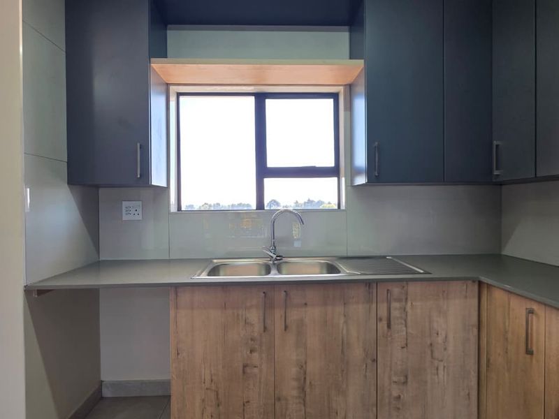 Modern kitchen featuring dark upper cabinetry, wood-look lower cabinets, stone countertops, and a double bowl sink with a window view.