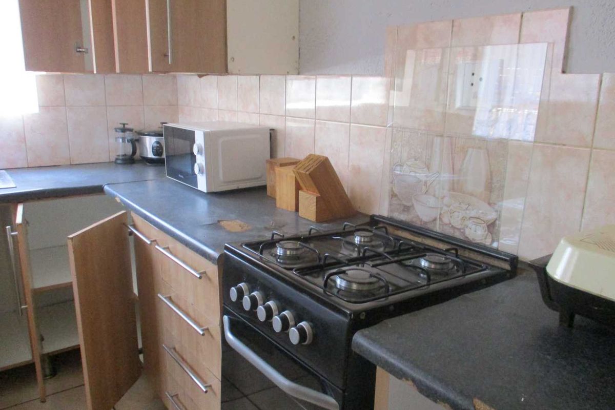 A dated kitchen featuring laminate countertops, tiled splashbacks, and a freestanding gas stove, currently showing signs of wear and maintenance requirements.