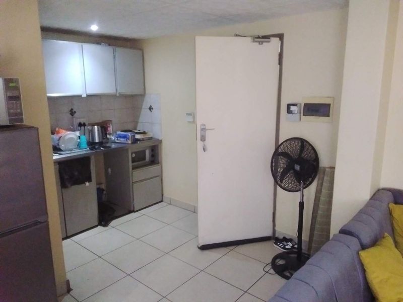 Open plan living area featuring a compact kitchenette with built-in cabinetry and tiled flooring throughout.