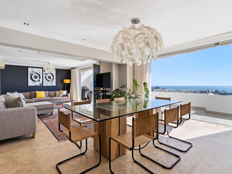 Spacious open-plan living and dining area featuring stone flooring, recessed lighting, and seamless access to a balcony with expansive ocean views.