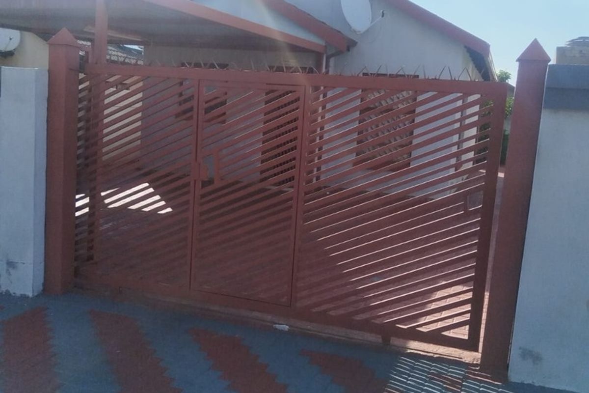 Front view of the property featuring a metal security gate, paved driveway, and an attached carport.