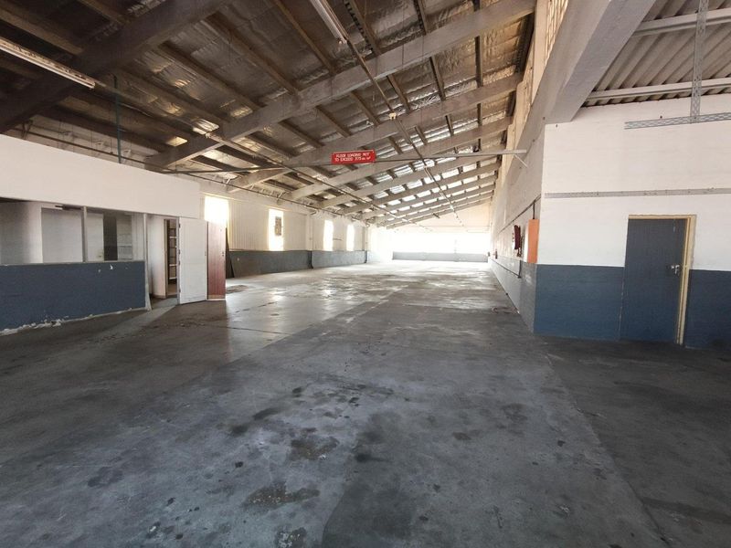 Spacious industrial warehouse unit featuring high ceilings with exposed steel trusses, concrete flooring, and functional open-plan layout suitable for storage or manufacturing.