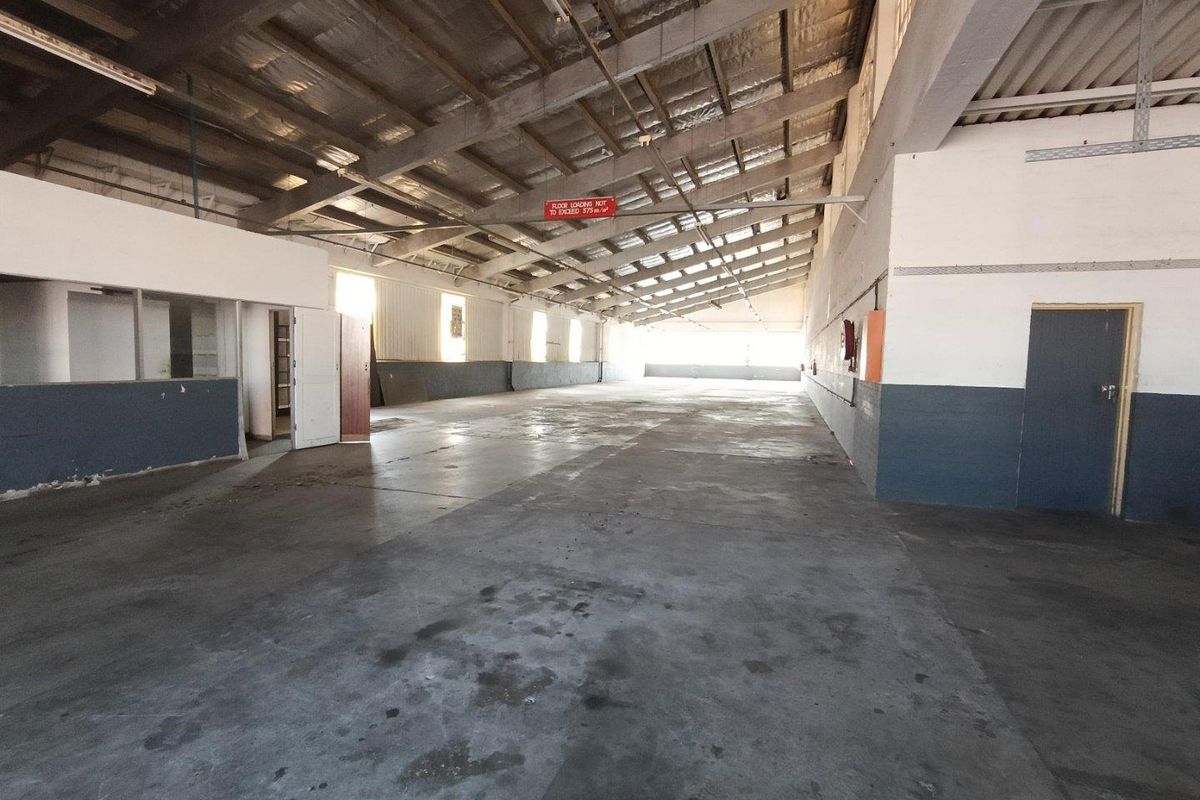 Spacious industrial warehouse unit featuring high ceilings with exposed steel trusses, concrete flooring, and functional open-plan layout suitable for storage or manufacturing.