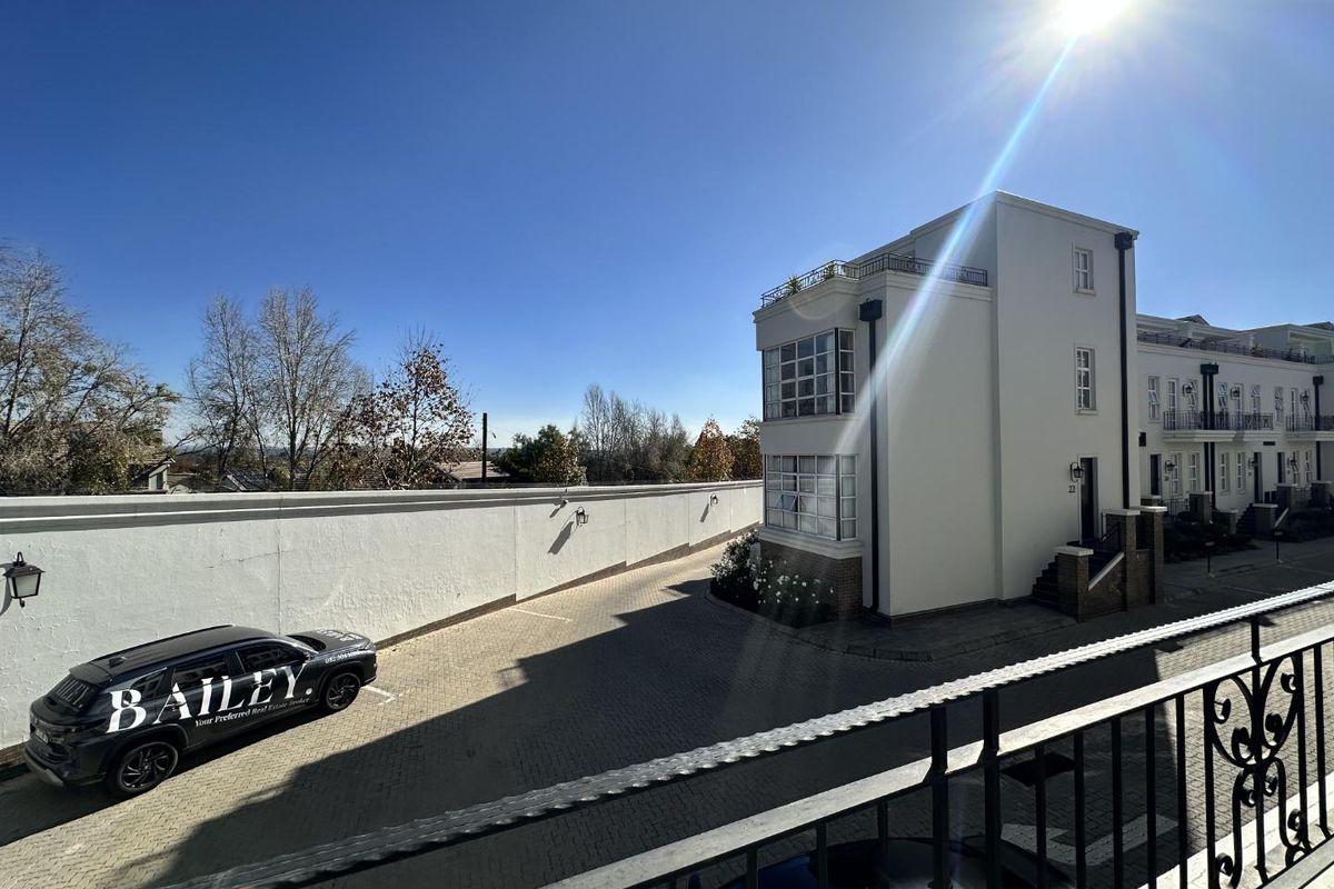 An elevated view of the townhouse complex exterior, featuring paved driveway, perimeter wall, and multi-story building architecture.