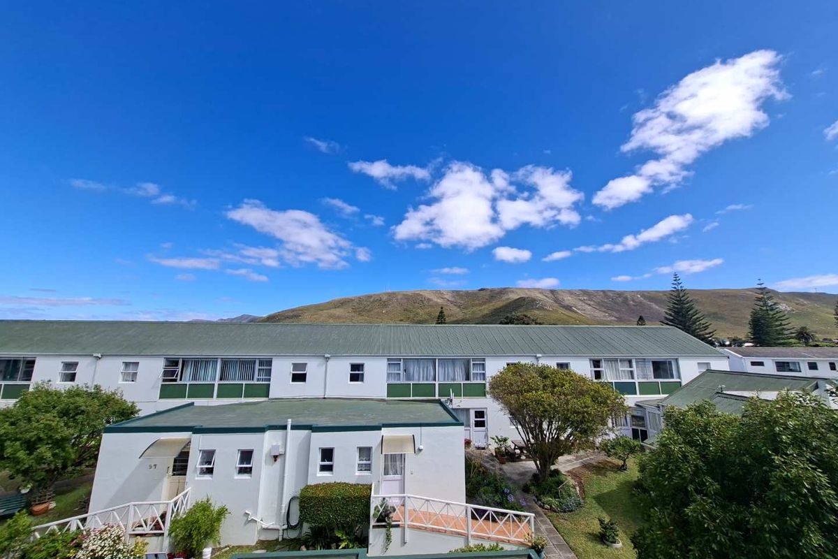 Exterior view of a multi-unit apartment complex featuring white facades, green pitched roofs, and landscaped garden areas with mountain views.