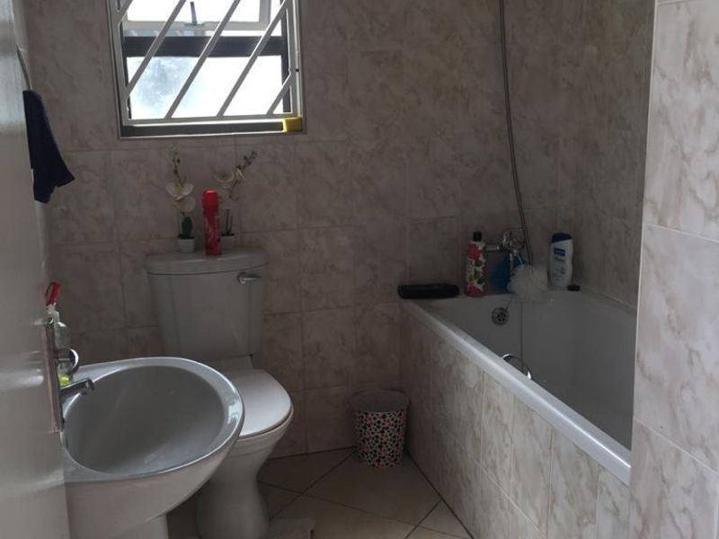 A functional bathroom featuring a pedestal basin, toilet, and a bathtub with a handheld shower attachment, finished with neutral wall and floor tiles.