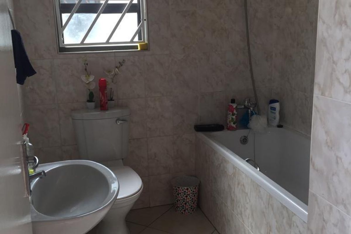 A functional bathroom featuring a pedestal basin, toilet, and a bathtub with a handheld shower attachment, finished with neutral wall and floor tiles.