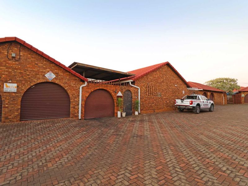 Front exterior view of a townhouse complex featuring face-brick facades, red tiled roofs, and a paved driveway with multiple garage access points.