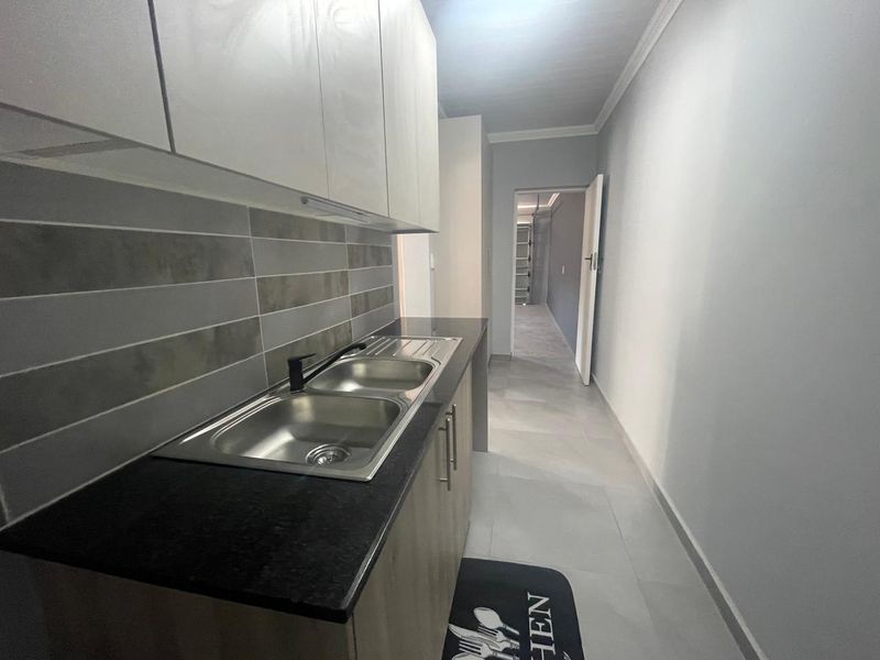 A clean and modern scullery area featuring double stainless steel sinks, contemporary cabinetry, and neutral tiled finishes, providing a functional secondary prep space.