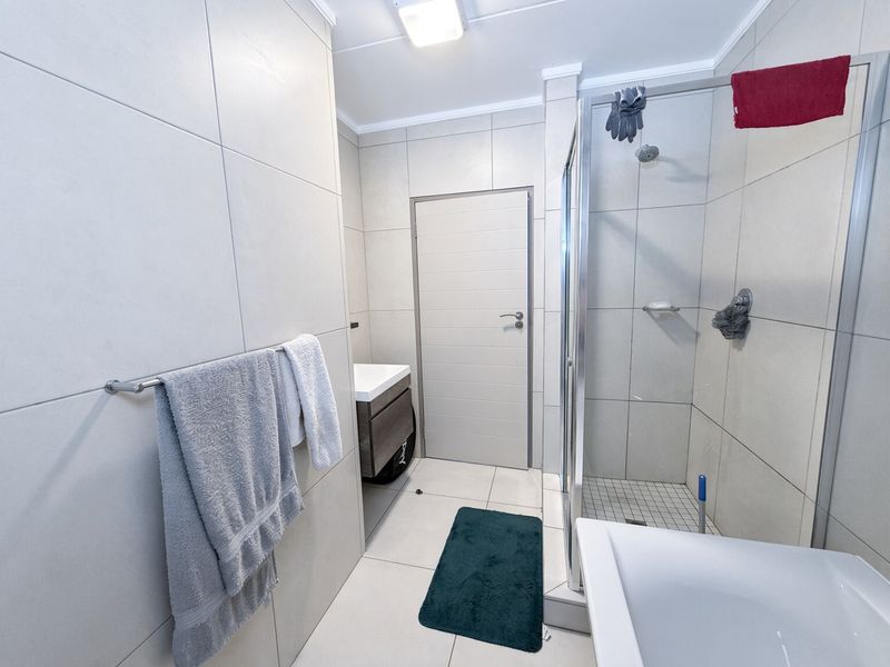 A modern bathroom featuring large format wall tiles, a glass-enclosed shower, and a contemporary wall-mounted vanity unit.