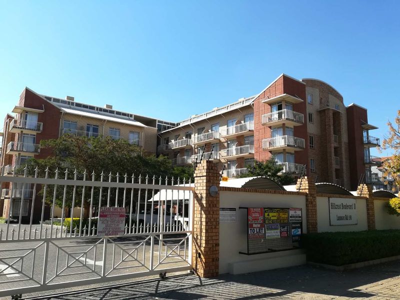 Front exterior view of Hillcrest Boulevard II apartment complex featuring brick facade, multiple balconies, and secure gated entrance.