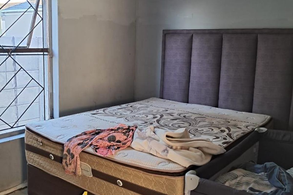 A bedroom featuring a window with a security gate, showing signs of wear on the walls and ceiling requiring maintenance and cosmetic updates.