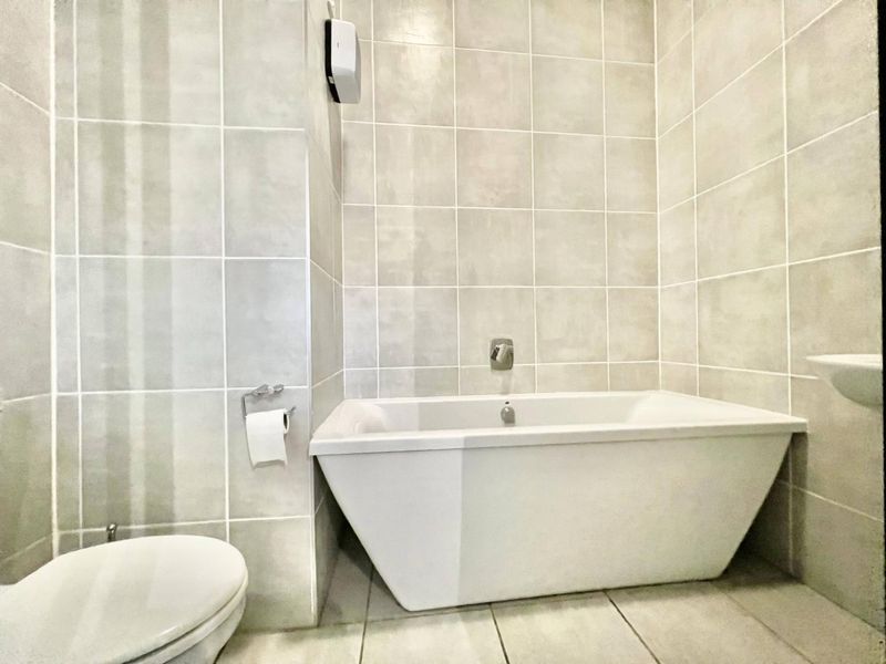 A clean, modern bathroom featuring neutral wall and floor tiling, a built-in bathtub, and a standard toilet.