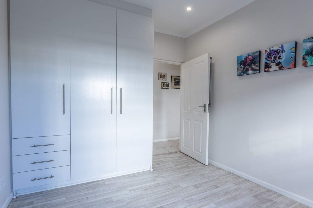 A bright bedroom featuring built-in white cabinetry with integrated drawers and light-toned wood-look flooring.