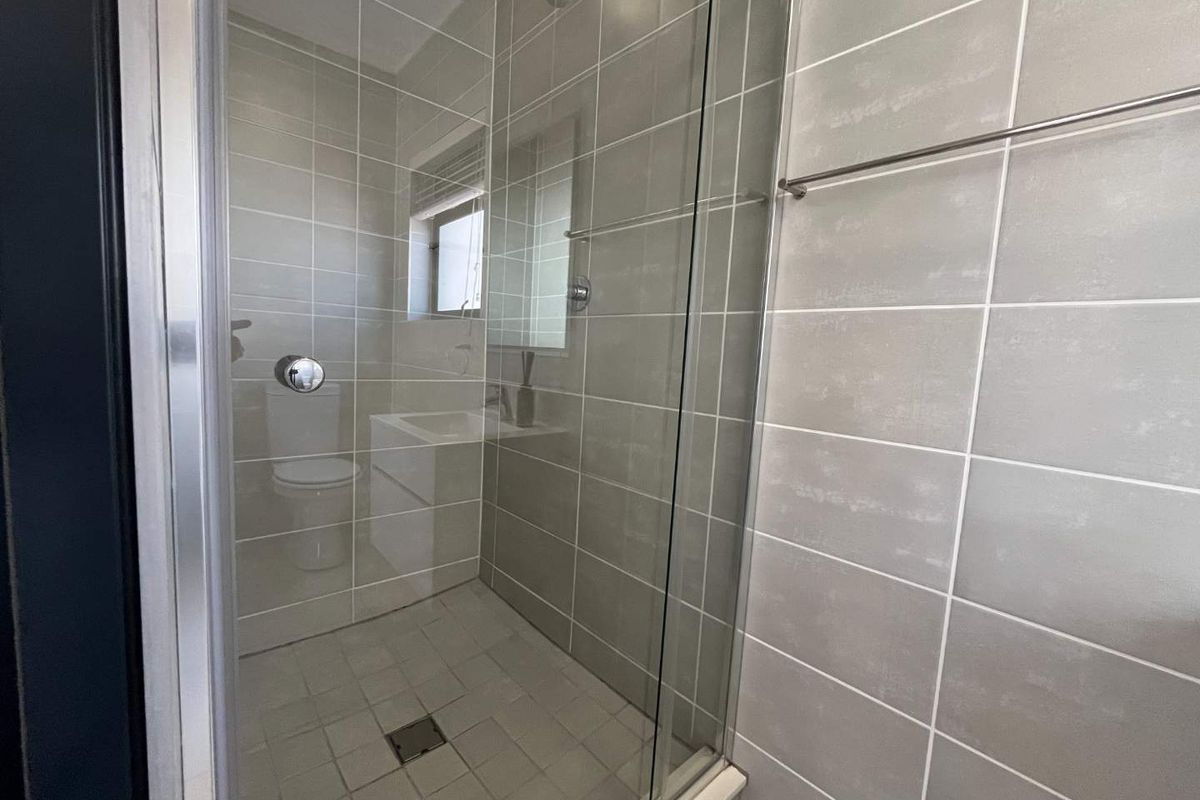 Modern bathroom featuring a glass-enclosed shower with neutral grey tiling, a wall-mounted shower head, and a clean, minimalist aesthetic.