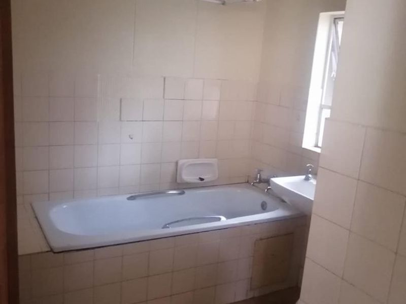A dated bathroom featuring a built-in bathtub, wall-mounted basin, and tiled walls, currently in need of cosmetic updates and renovation.