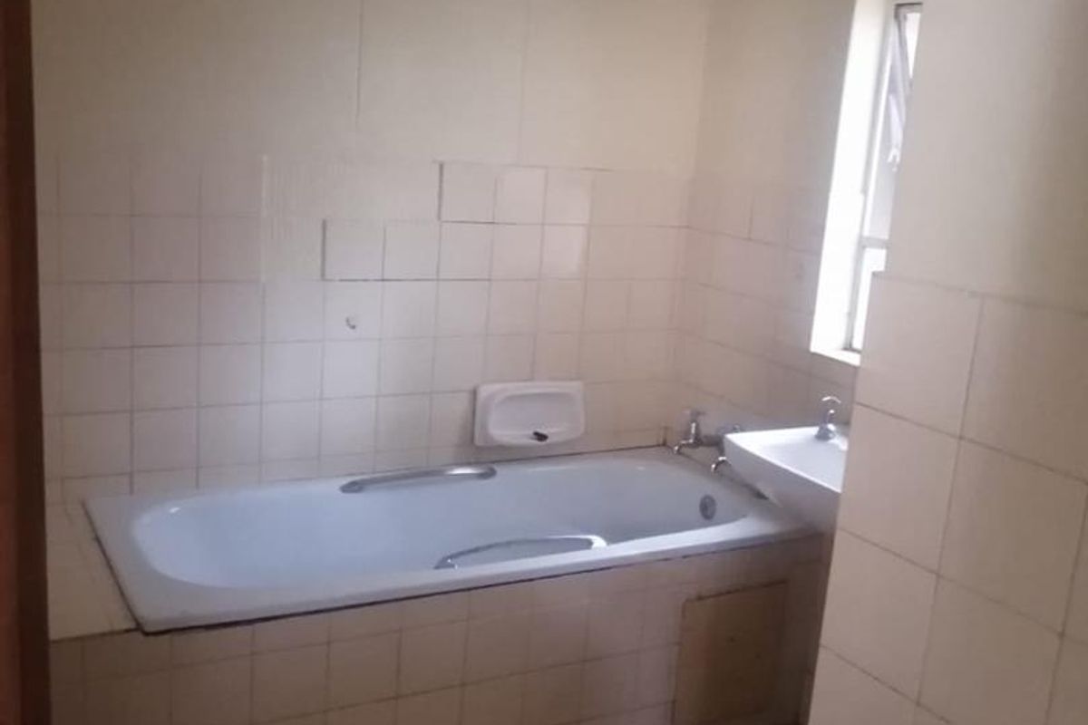 A dated bathroom featuring a built-in bathtub, wall-mounted basin, and tiled walls, currently in need of cosmetic updates and renovation.