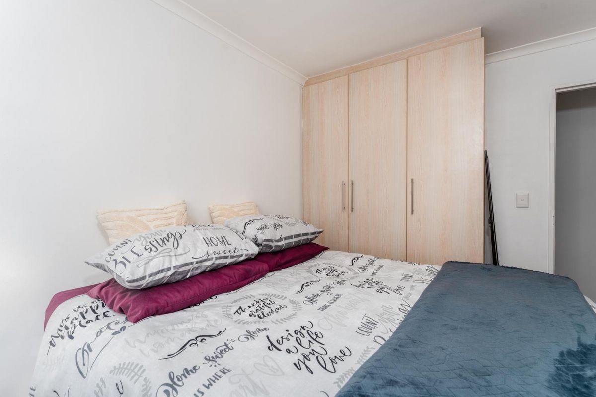 A well-maintained bedroom featuring built-in light wood-grain wardrobes and neutral wall finishes.