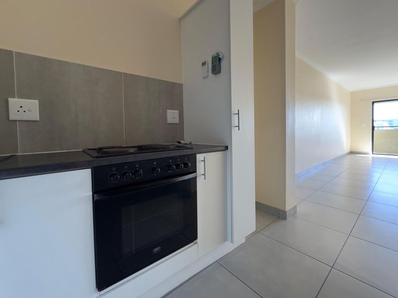 A clean, modern kitchen area featuring built-in cabinetry, an integrated oven and hob, and neutral tiled flooring, leading into an open-plan living space.