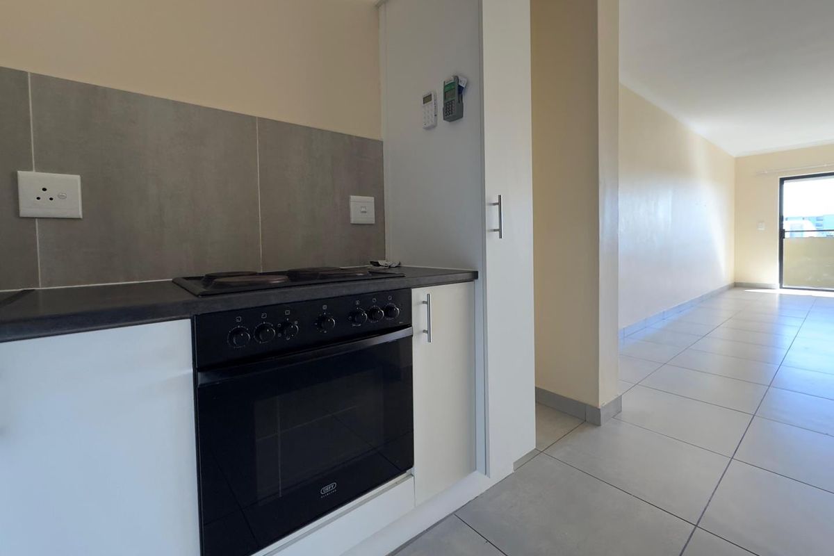 A clean, modern kitchen area featuring built-in cabinetry, an integrated oven and hob, and neutral tiled flooring, leading into an open-plan living space.